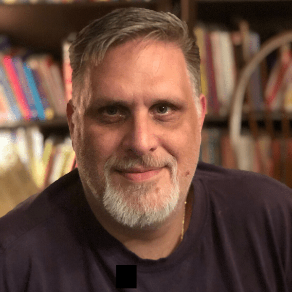 A man with a beard in front of a bookshelf.