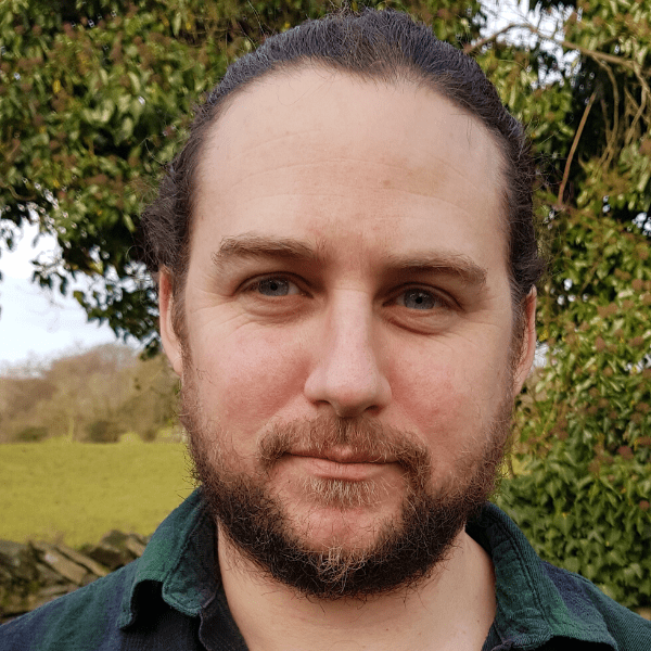 A man with a beard standing in front of a tree.