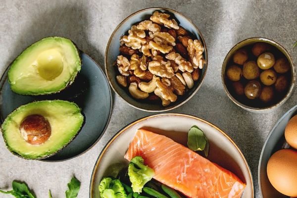 Bowls and plates containing avocado, eggs, nuts and salmon.