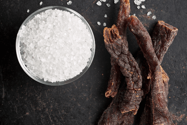 A bowl of salt and pieces of beef jerky.