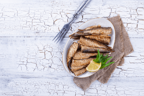 Fish and a slice of lemon on a white dish with a fork.