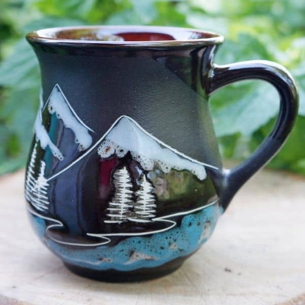 A black mug with mountains and trees on it.