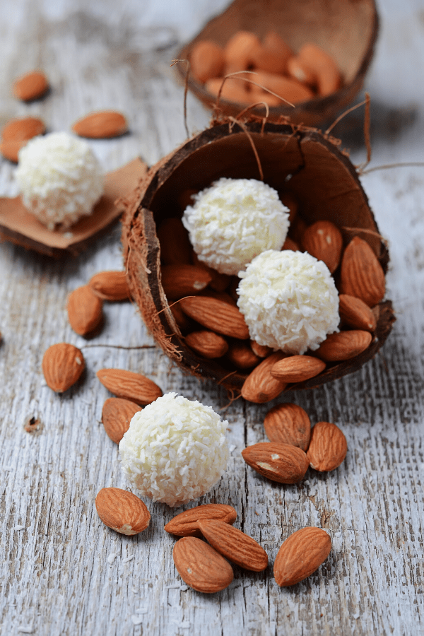 No-bake coconut keto fat bomb garnished with almond nuts on a white-painted wooden table.