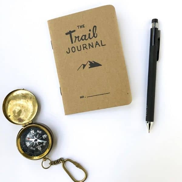 A brown journal, pen, and a compass on a white surface.