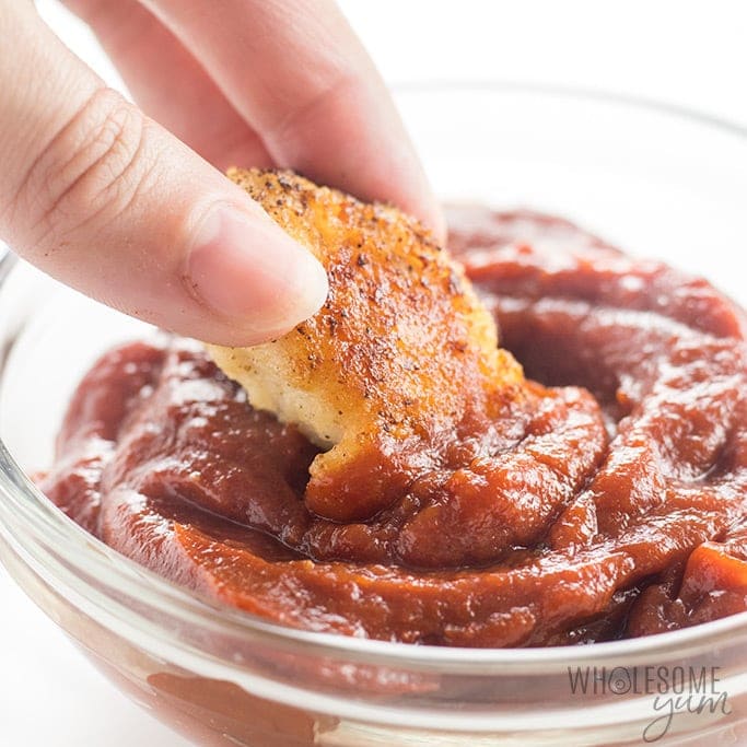 A person enjoying a piece of bread and a bowl of sauce.
