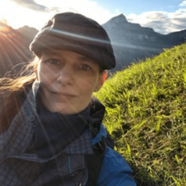 A woman in a hat is taking a selfie in the mountains.