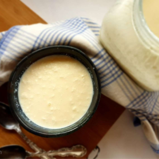 A bowl of homemade raw milk yogurt on a wooden board with two spoons next to a jar of it.