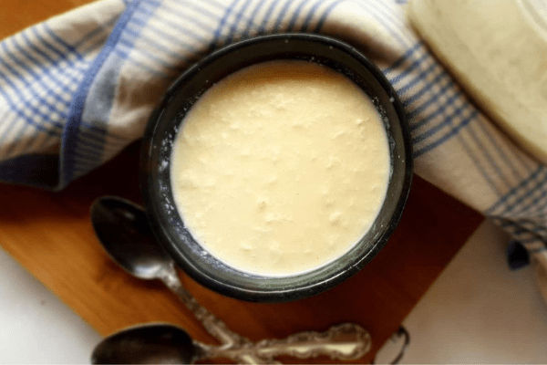 A bowl of homemade raw milk yogurt on a wooden board with two spoons.