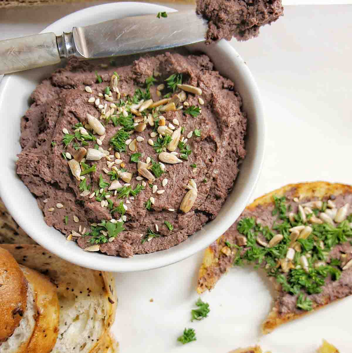 A bowl of chicken liver pate next to a slice of bread with a bite.