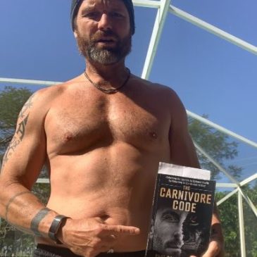 A shirtless man holding up a book.