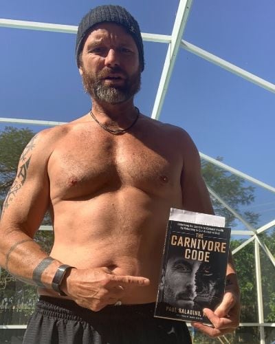 A shirtless man holding up a book.