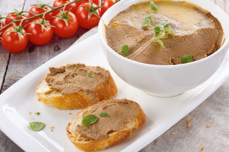 Chicken liver pate in a bowl next to two slices of bread.