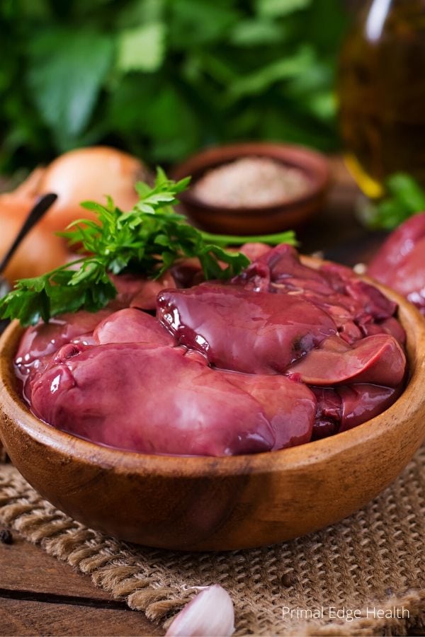 Chicken liver in a wooden bowl next to spices and ingredients.