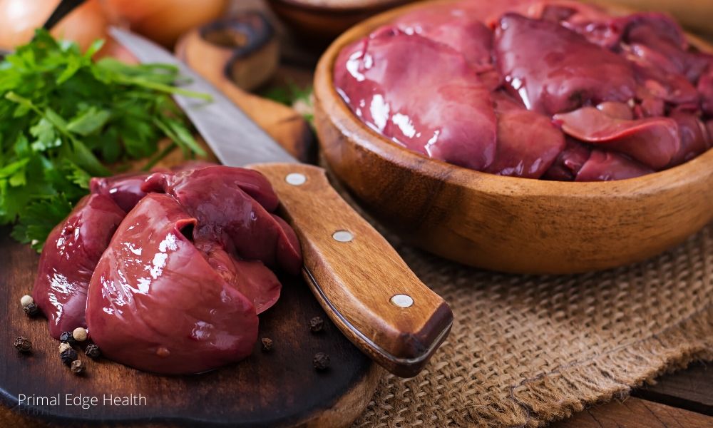 Chicken liver on a wooden bowl and some pieces on a wooden board next to a knife.