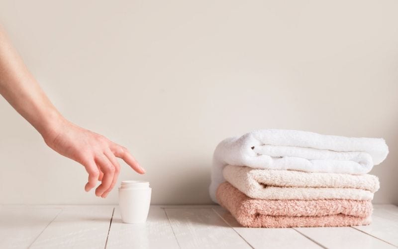 A person about to dip a finger into a white bottle of tallow.