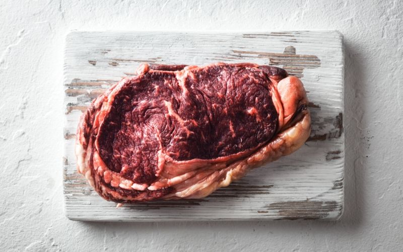 A piece of raw meat on top of a wooden chopping board.