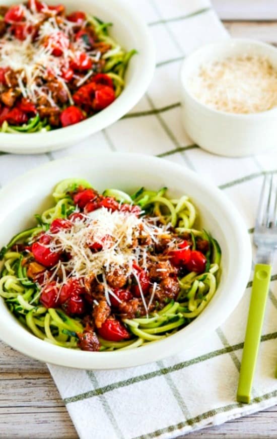 Two bowls of zucchini noodles with cherry tomato sauce and cheese.