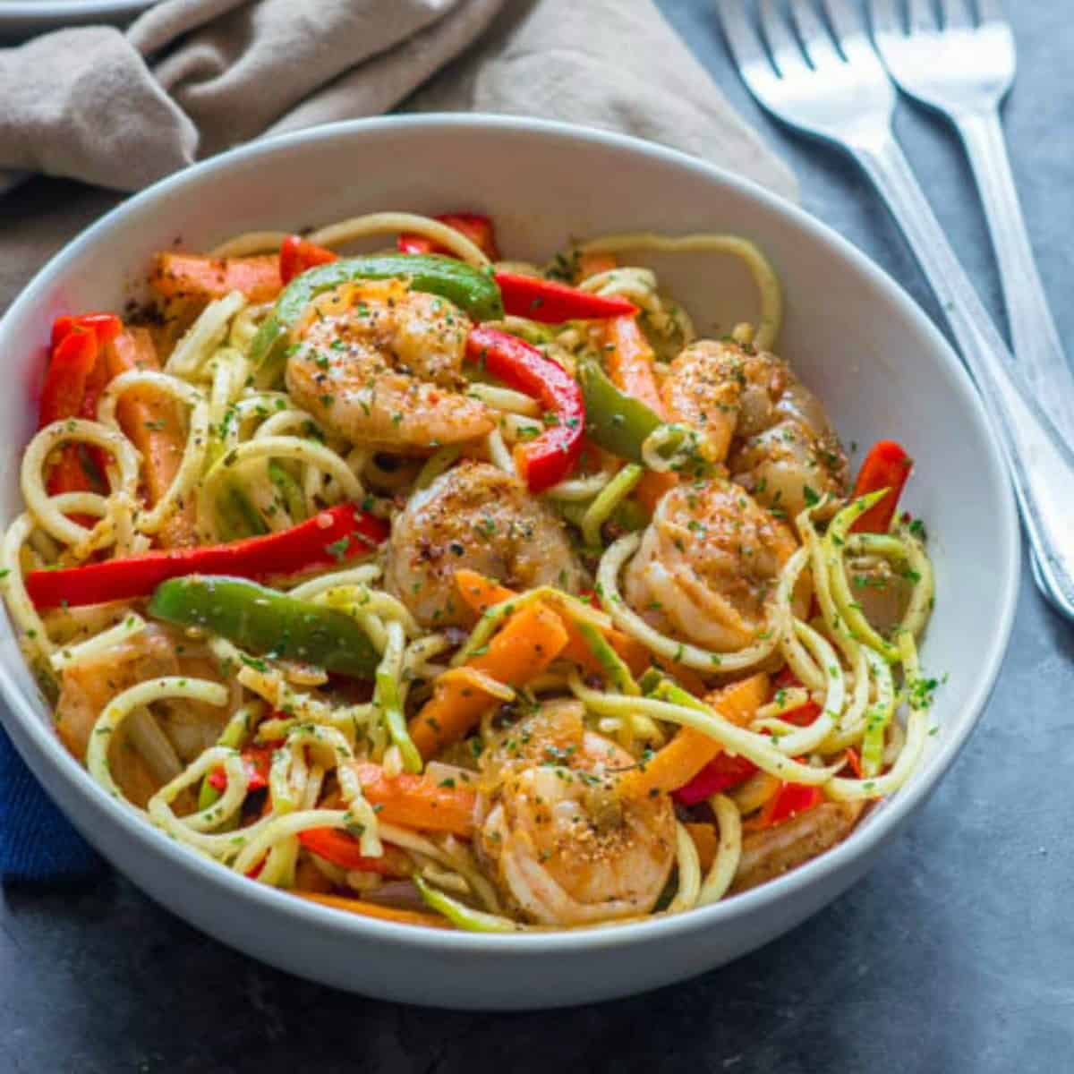 Cajun shrimp with zoodles in a white bowl next to two forks.