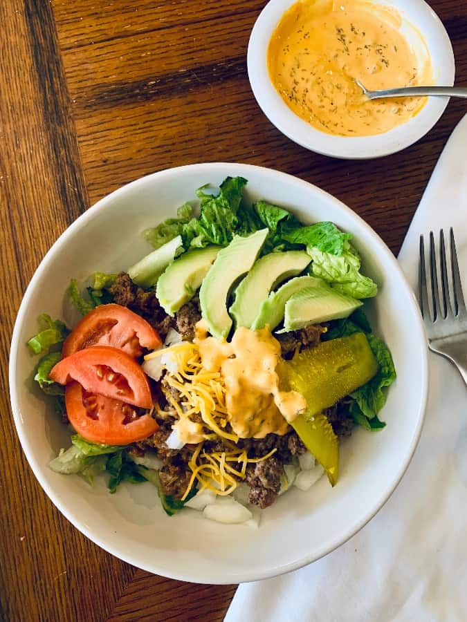 Low-carb cheeseburger salad in a white bowl on a wooden surface.