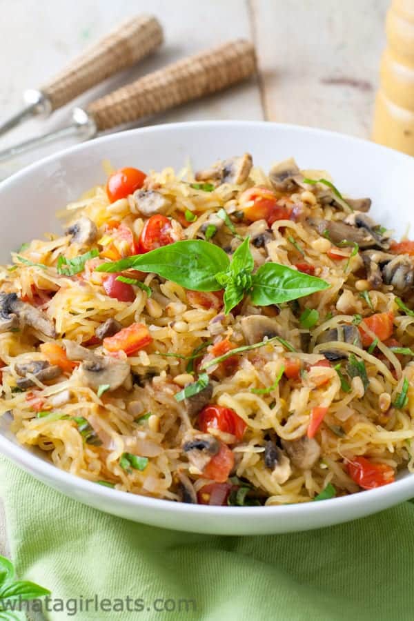 Spaghetti with squash, mushrooms and tomatoes in a white bowl.