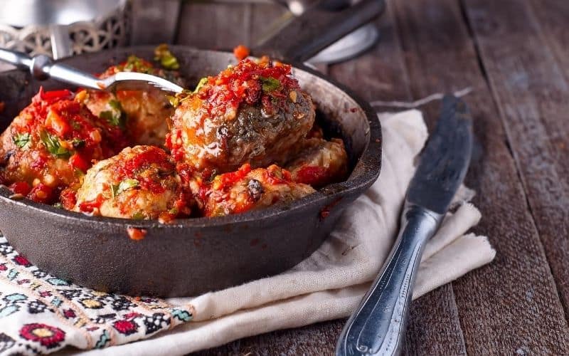 Keto Turkish meatballs made with ground beef sizzling in a skillet on a rustic wooden table.