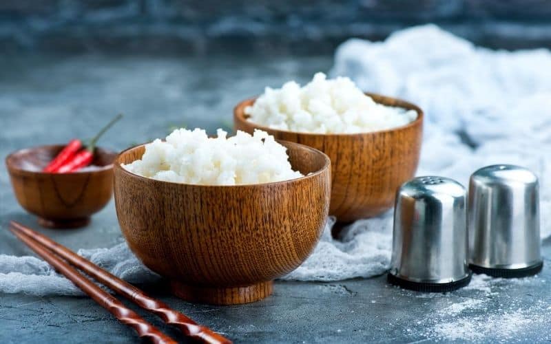 Bowls of cauliflower rice next to salt and pepper and a bowl with chilis.