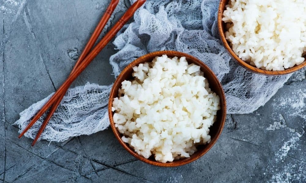 Two bowls of cauliflower rice next to a pair of chopsticks.