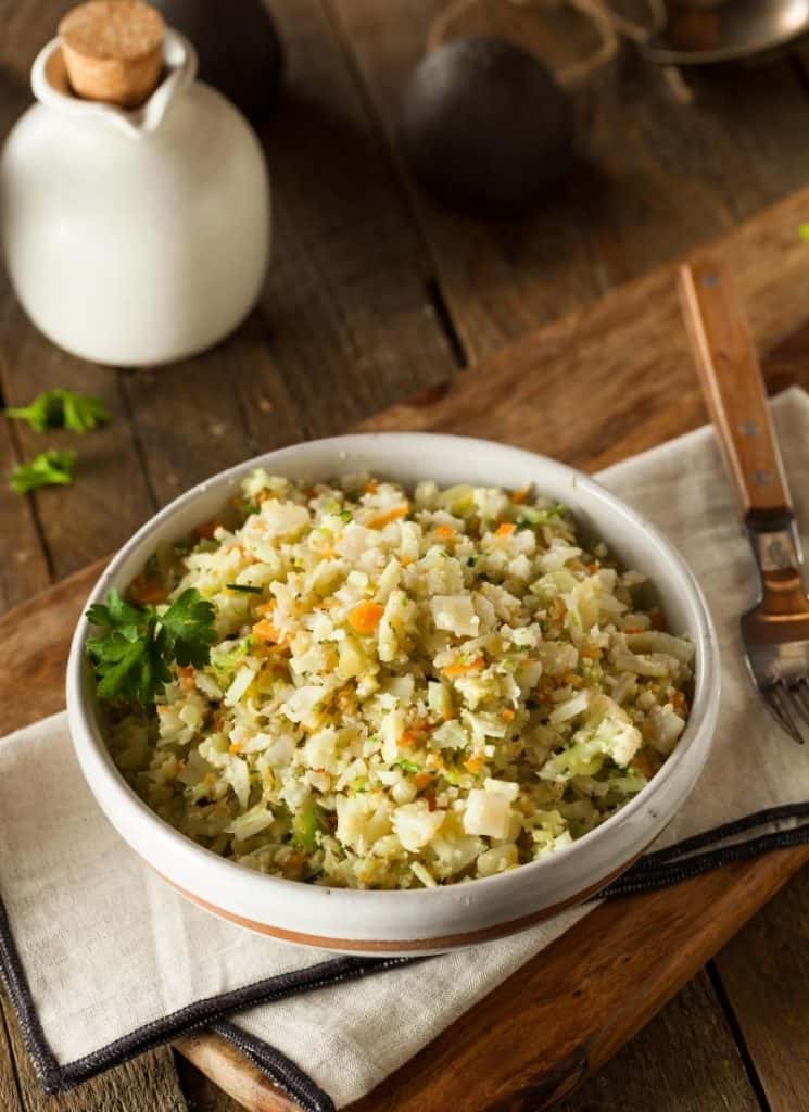 Cooked cauliflower rice in a bowl next to a spoon.