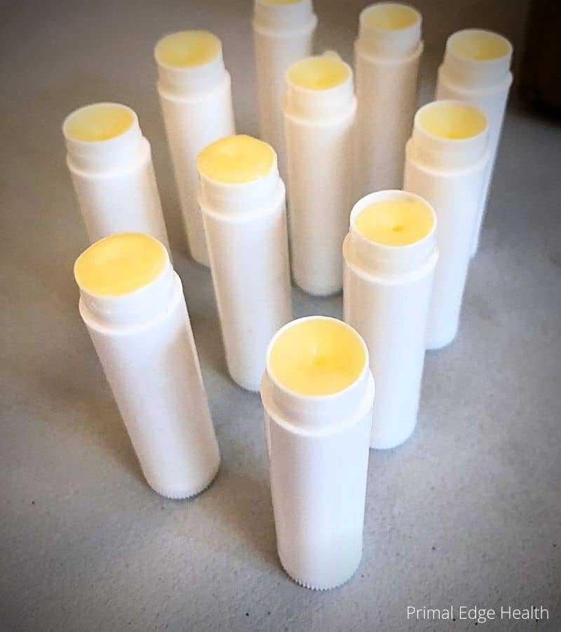 A group of white lip balm bottles with white lids sitting on a concrete floor.