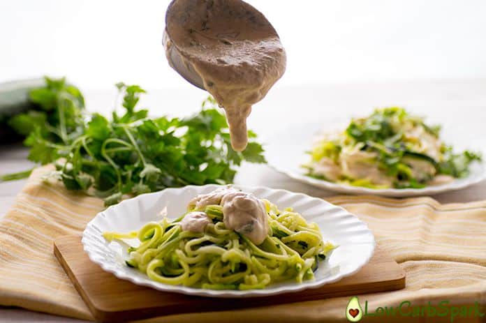 Keto Alfredo sauce being poured on zucchini keto noodles.