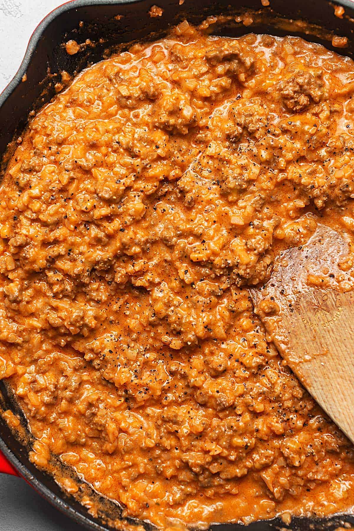 A skillet filled with meat sauce and a wooden spoon.