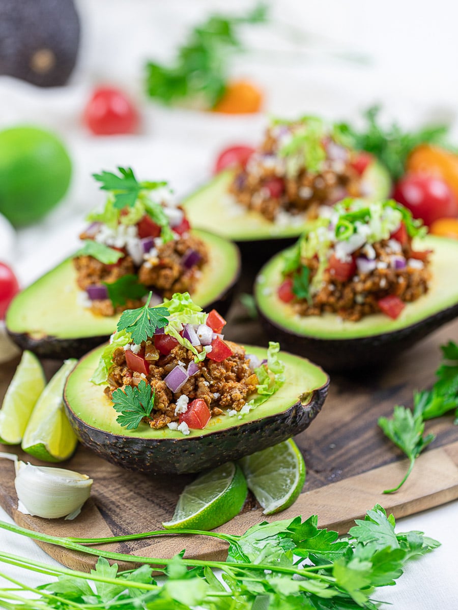 Keto taco stuffed avocado boats on a wooden board.