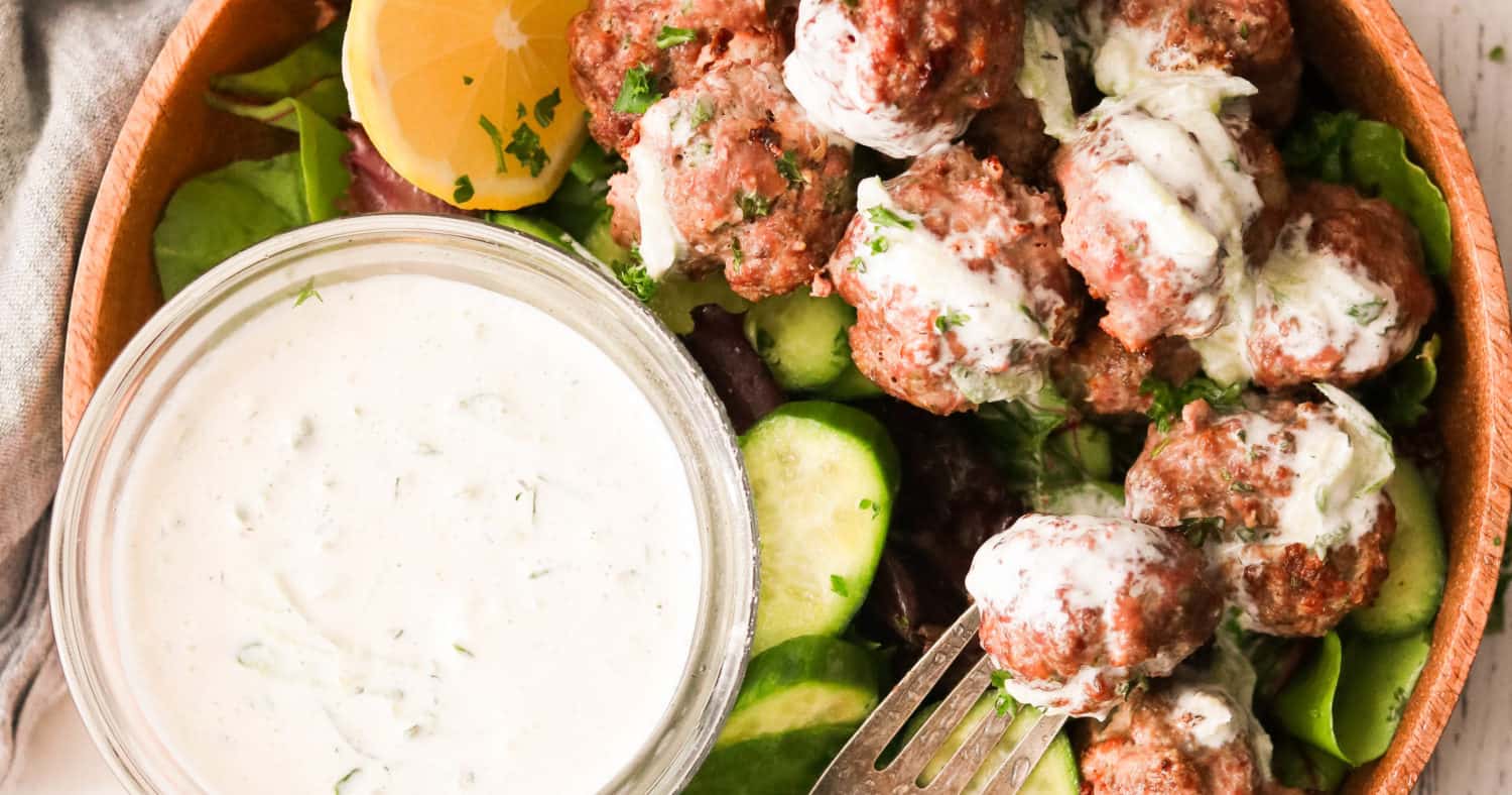 Meatballs in a bowl with white dipping sauce and vegetables.