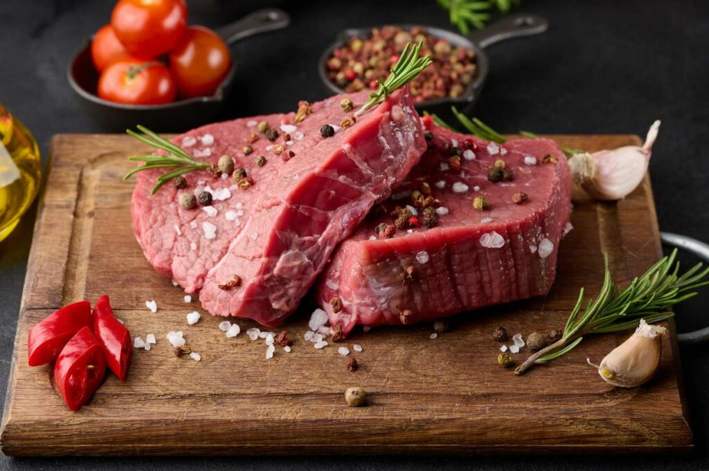 Raw beef on a cutting board seasoned with herbs, spices, and coarse sea salt.