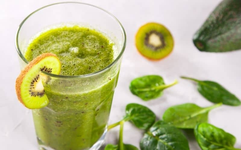 Green smoothie in a glass garnished by a slice of kiwi fruit.