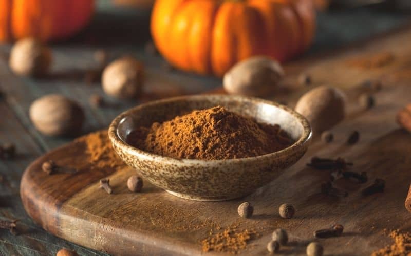 Pumpkin spice in a small brown container on a wooden board.