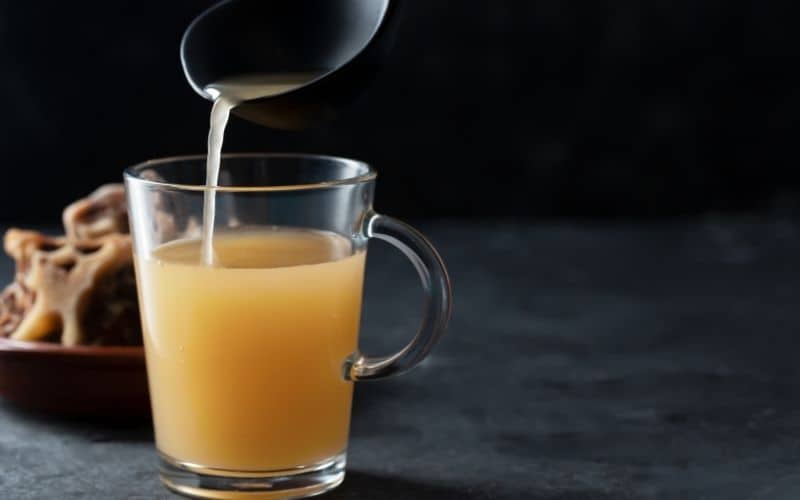 A liquid from a ladle being poured in a transparent mug.