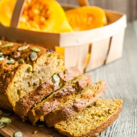 Pumpkin bread on a wooden board with a basket of pumpkin behind.