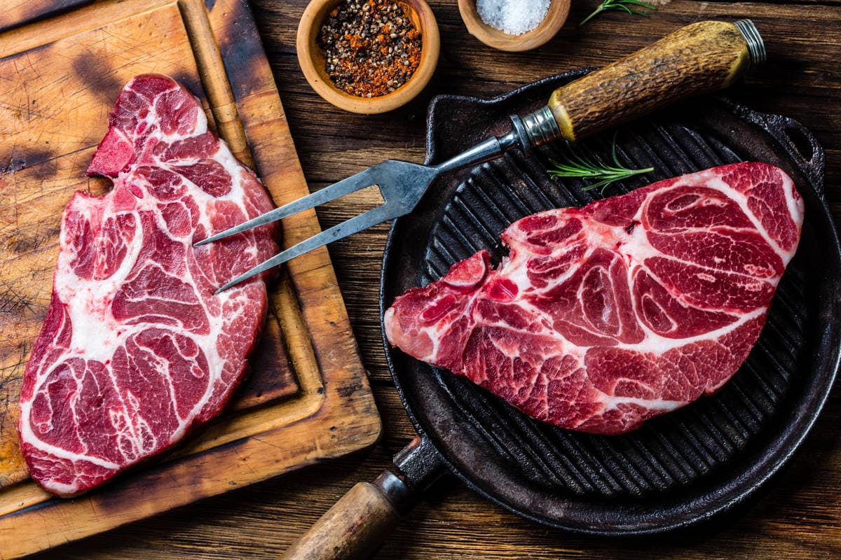 Two pieces of steak on a wooden surface.