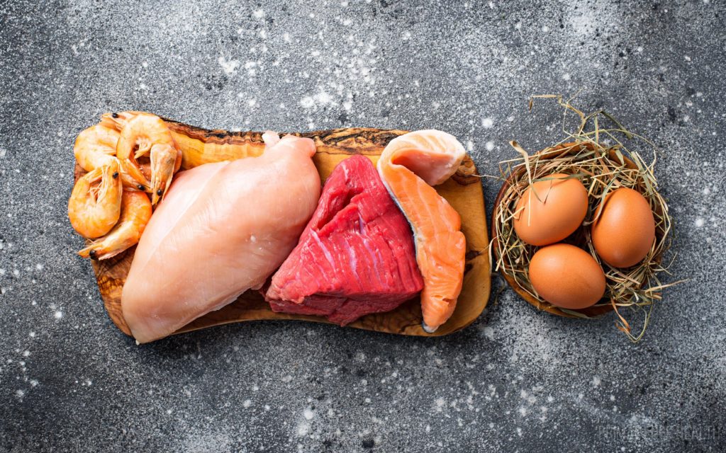 Raw meat, shrimps and eggs on a grey surface.