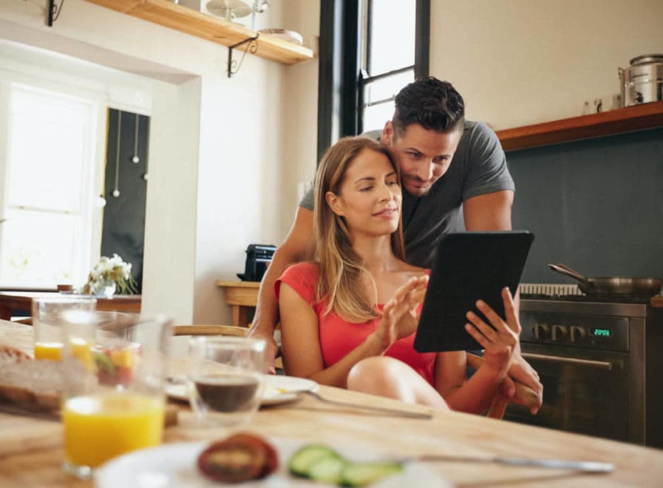 A man and a woman looking at an electronic device in the kitchen.