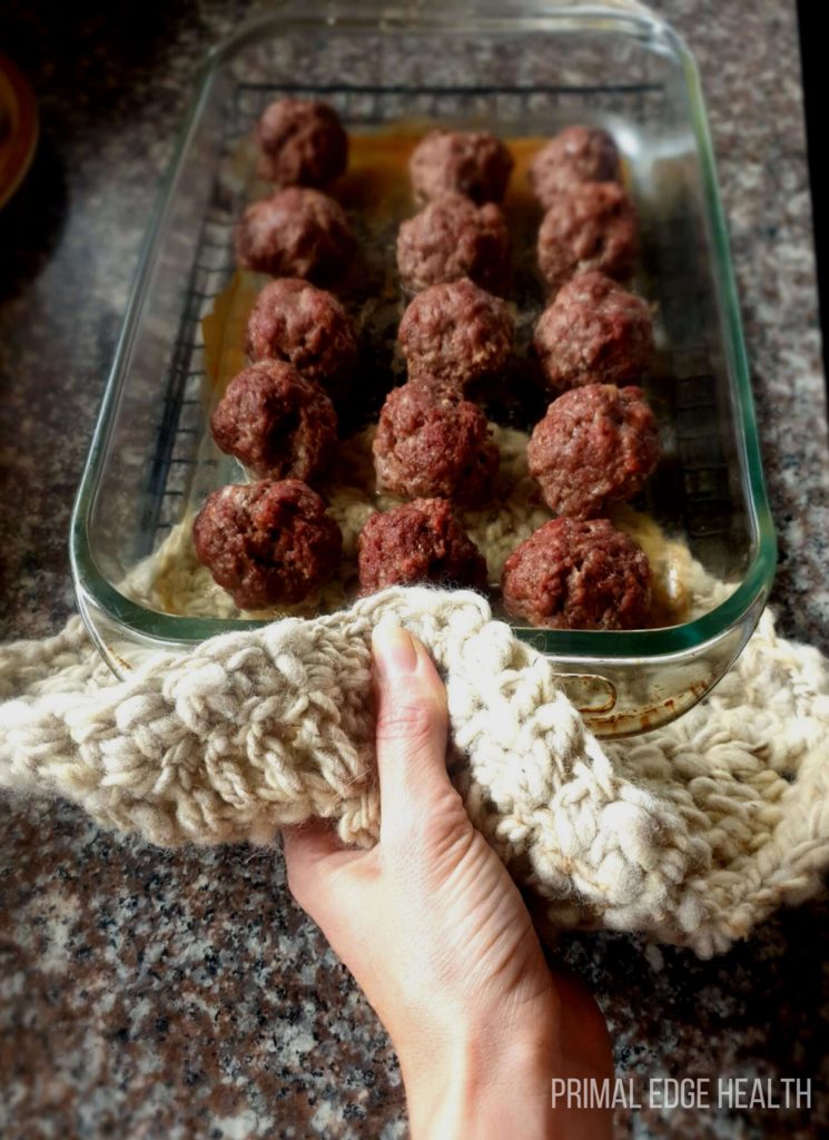 A person's hand holding a glass dish of carnivore meatballs.