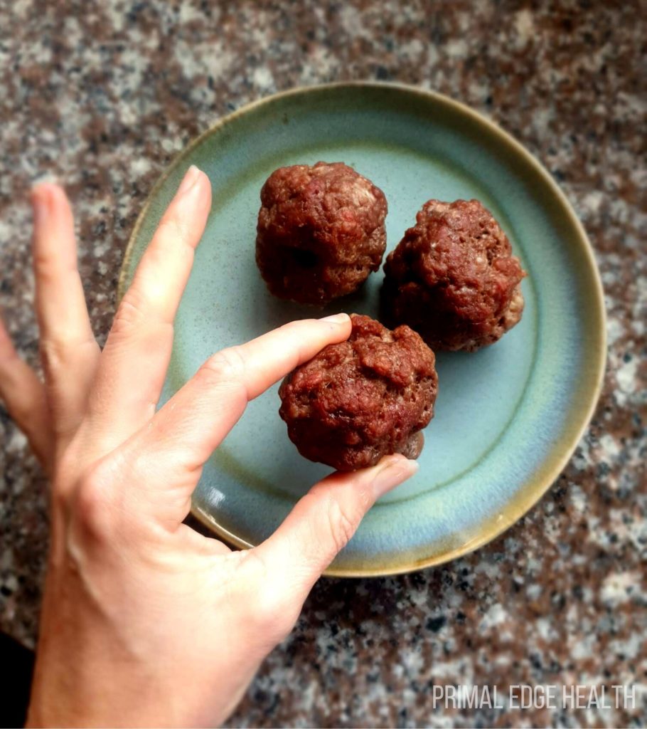 2 meatballs on a blue plate and a person's hand holding 1 up.