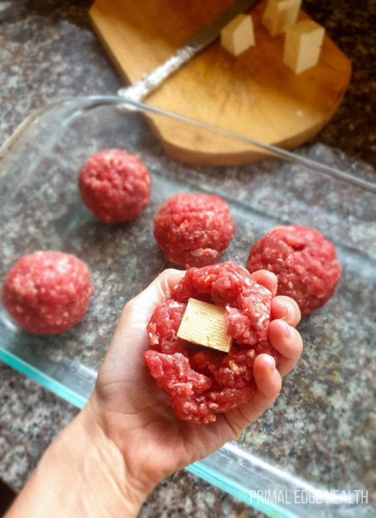 Meatballs in a glass dish and a person's hand holding one up stuffed with cheese.