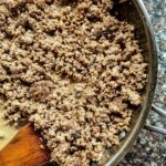 Ground beef in a pan with a wooden spoon.