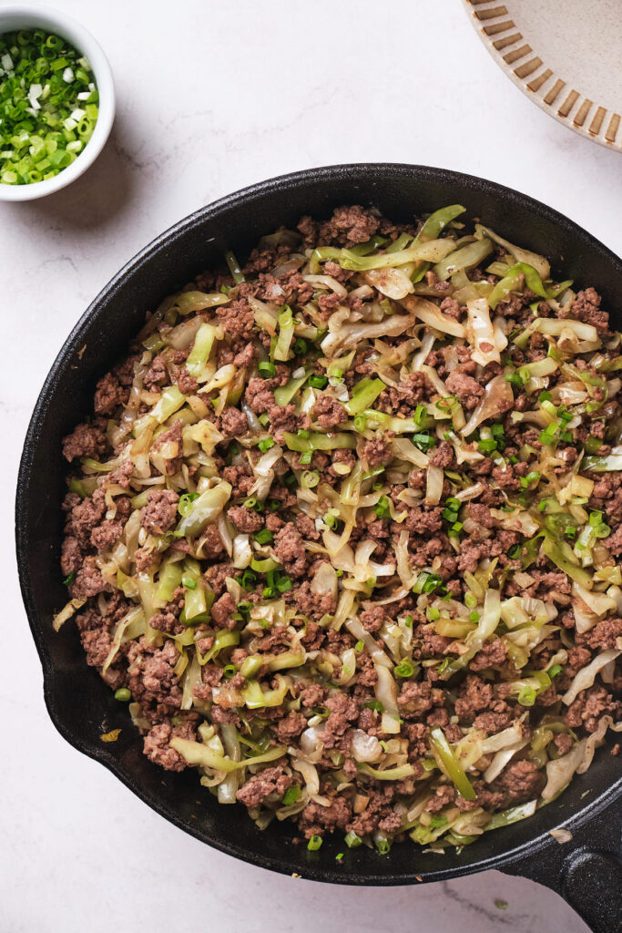 Cooked ground beef and cabbage stir fry in a black skillet.