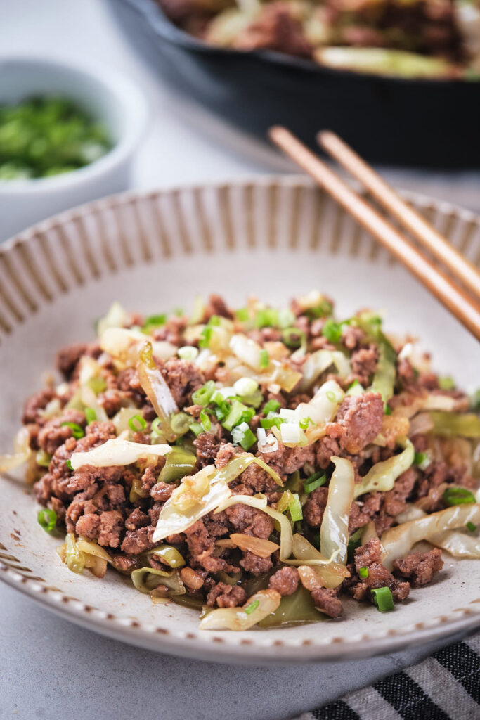 A bowl of stir-fried minced meat with chopped green onions and cabbage.