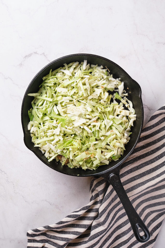 A cast iron skillet filled with shredded cabbage for a stir fry.