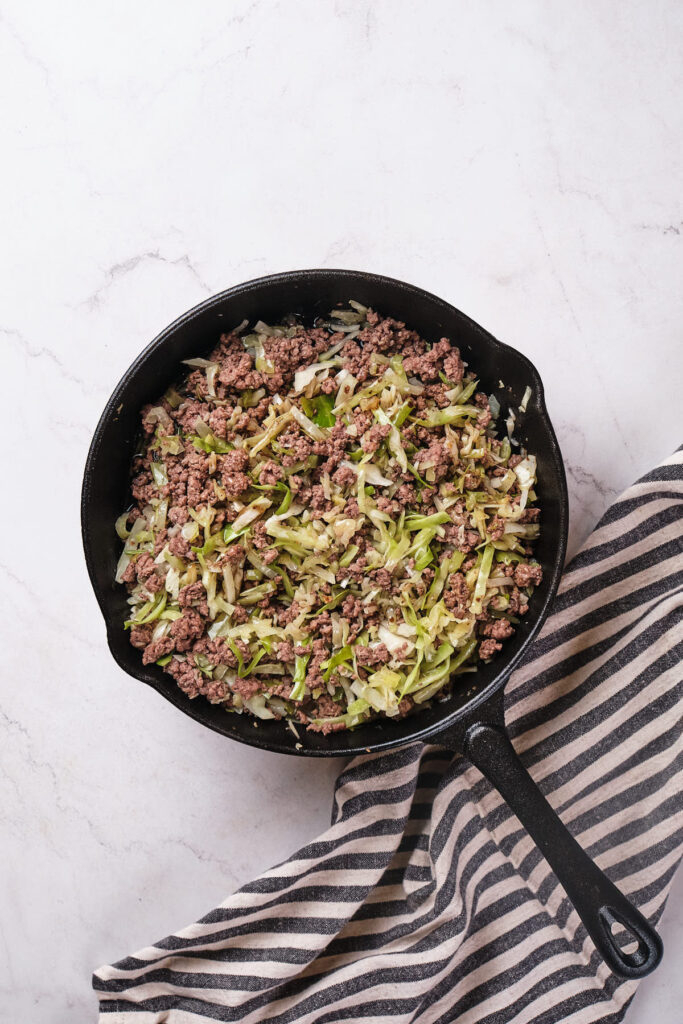 A cast iron skillet containing cooked ground beef and shredded cabbage stir fry.