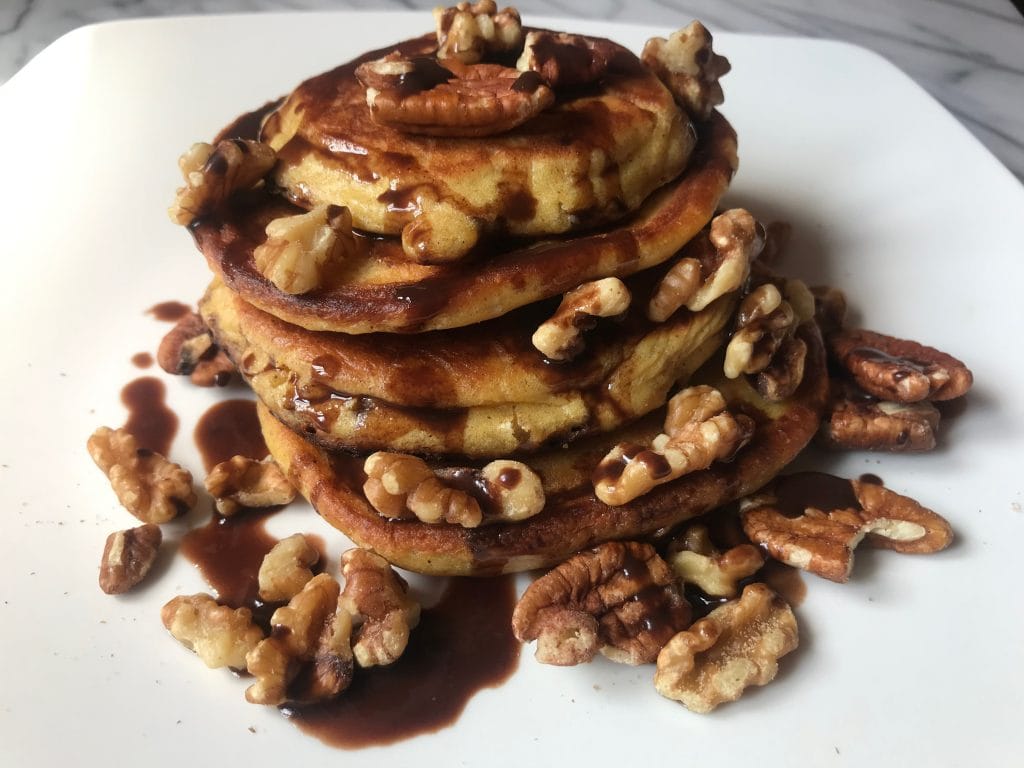 A stack of pancake with syrup and nuts.